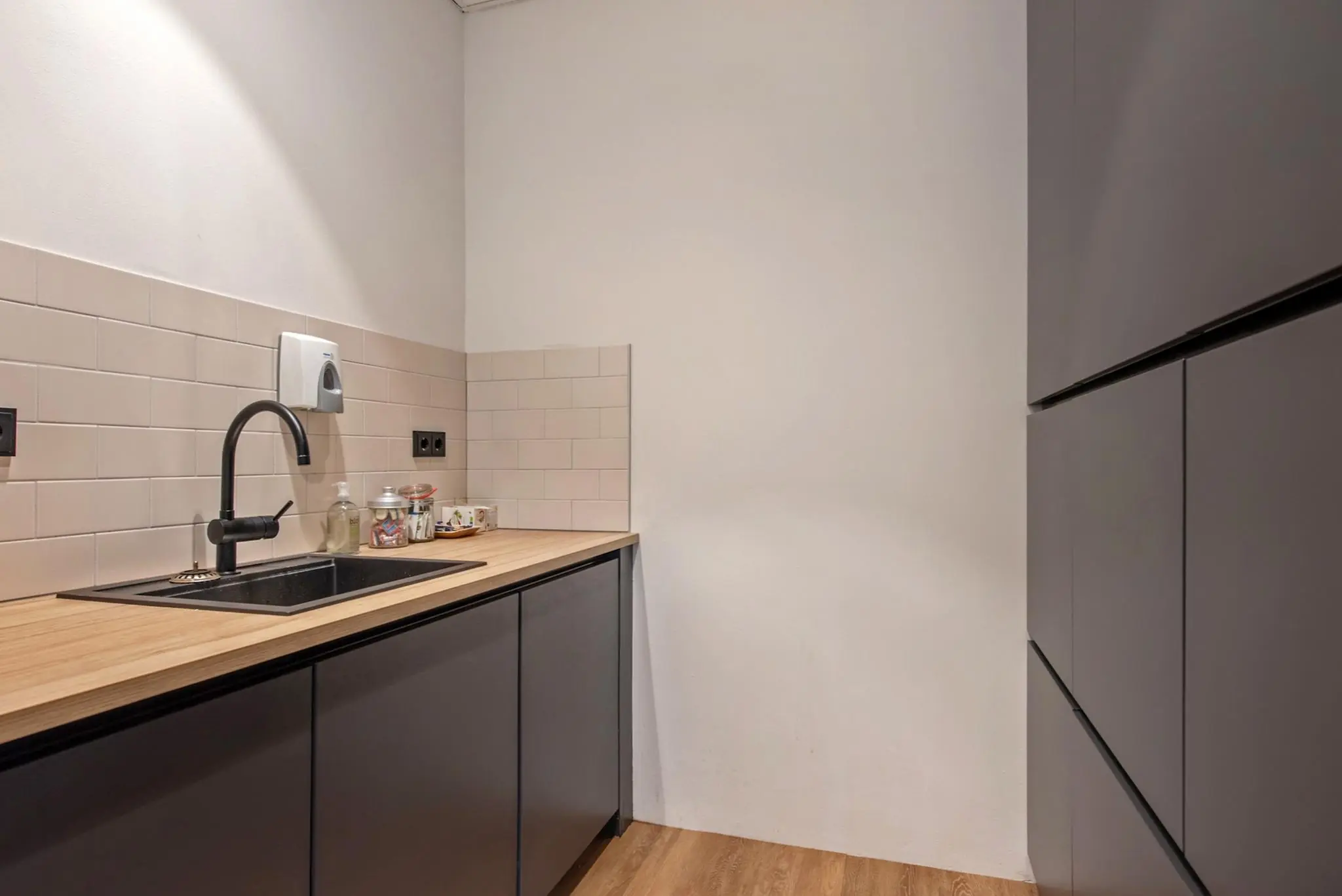 Moderne kitchenette met zwart aanrechtblad, houten werkblad en lichte tegelwand in een ruimte aan de Grote Marktstraat.